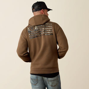 A man viewed from behind wearing a brown hooded sweatshirt with a distressed American flag graphic and the brand name ARIAT on the back. 
