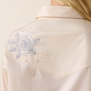 Close-up of a beige shirt with blue floral embroidery on the back.