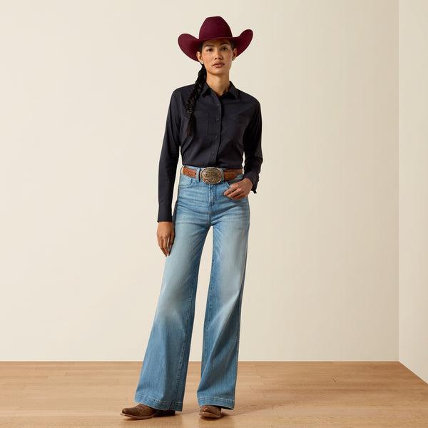 A woman wearing a black long-sleeve button-up shirt and a burgundy cowboy hat, looking down against a plain beige background.
