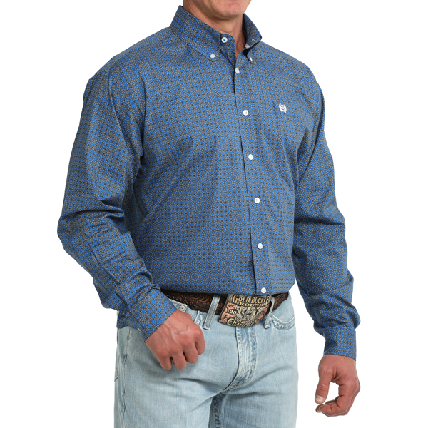 A man wearing a blue long-sleeve button-down shirt with a small geometric pattern, paired with light-wash jeans and a western belt, shown from the waist up against a white background.
