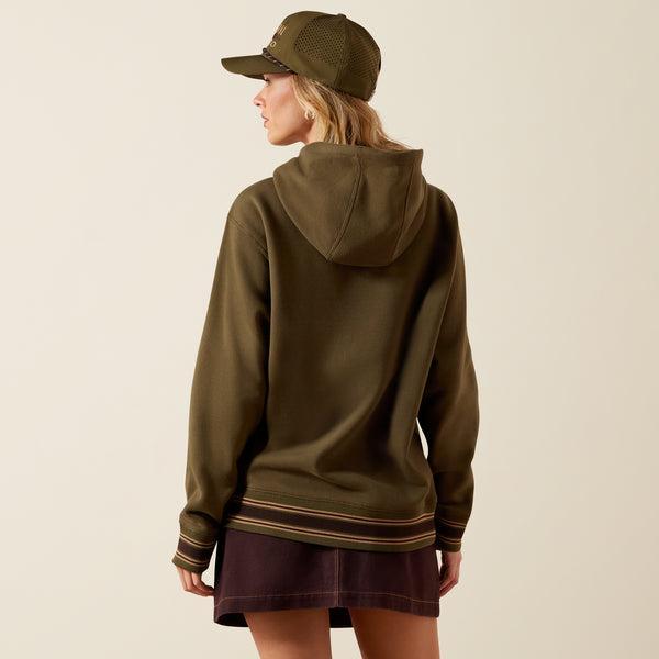 A woman wearing an olive green pullover hoodie with drawstrings, a kangaroo pocket, and ribbed cuffs and hem with thin tan stripes. 