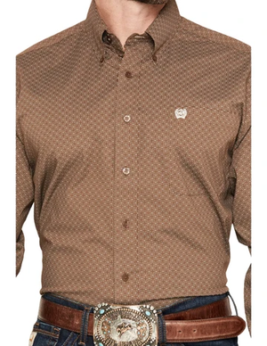 A man wearing a brown long-sleeve button-down shirt with a small white geometric pattern, paired with a brown leather belt and a large western-style silver buckle.