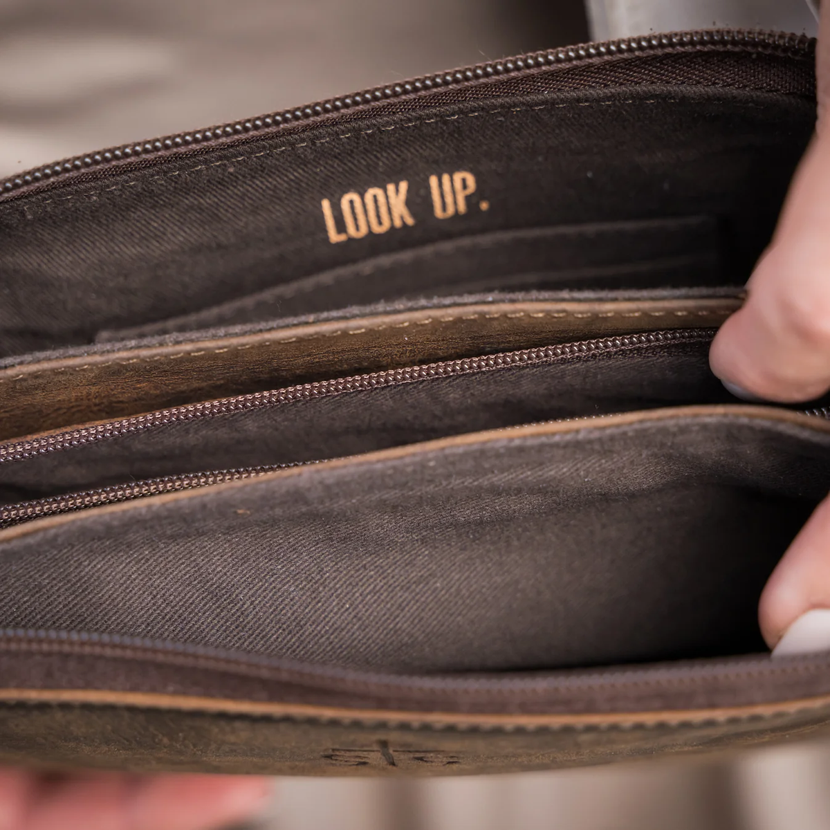 Close-up of an open brown leather wallet or clutch showing interior compartments, stitching, and the brand name 'LOOK UP.' printed in tan on the lining.
