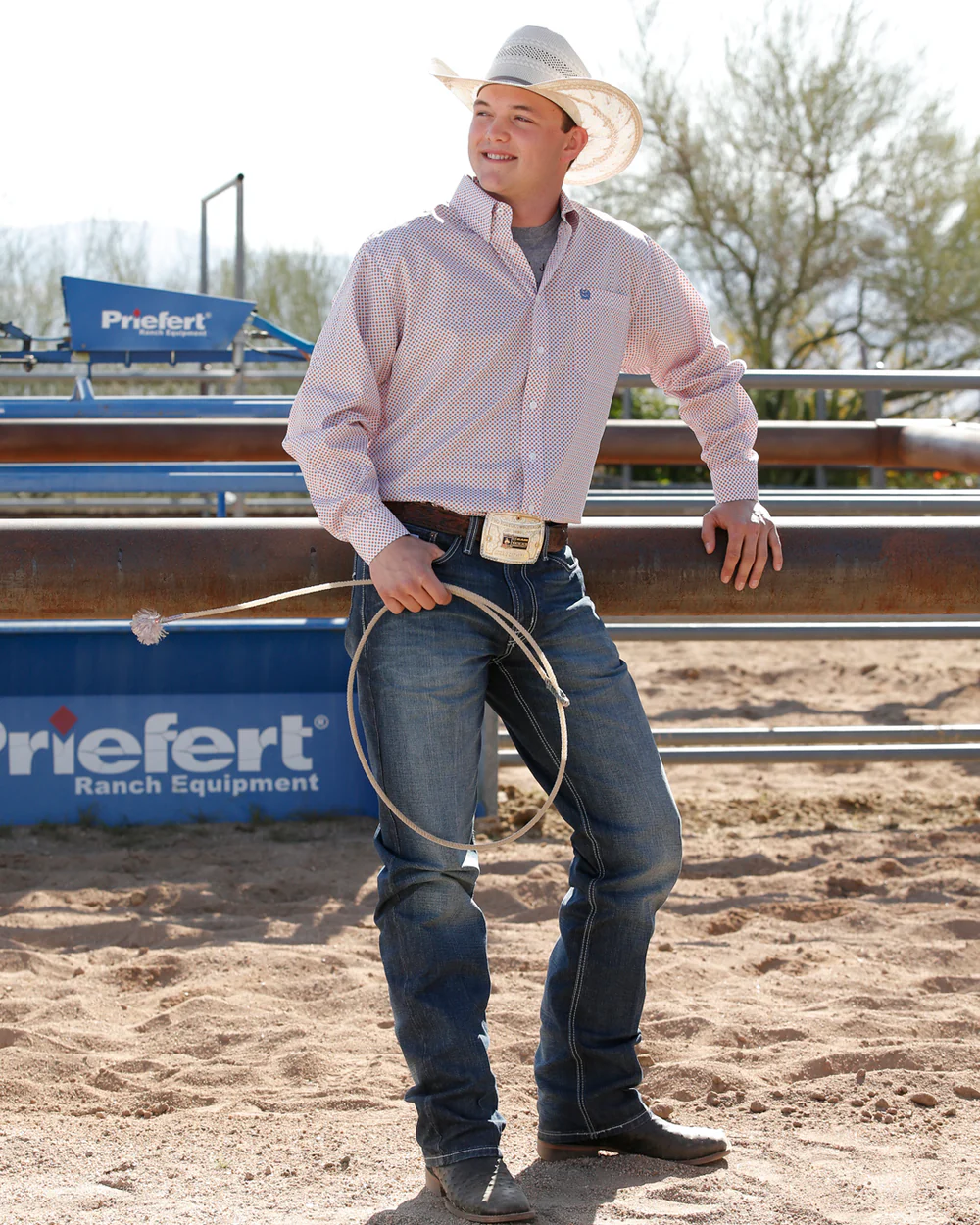 Man in cowboy attire holding a lasso in an outdoor setting with 'Friefert Ranch Equipment' branding.