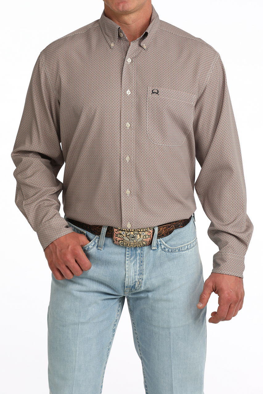 A man wearing a long-sleeve button-down shirt with a small-scale geometric pattern in taupe and beige, paired with light blue jeans and a western belt.