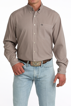 A man wearing a long-sleeve button-down shirt with a small-scale geometric pattern in taupe and beige, paired with light blue jeans and a western belt.