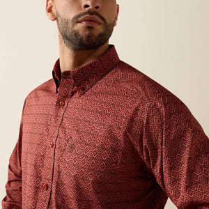 A close-up of a man wearing a long-sleeve button-down shirt with a textured geometric pattern in dark red and brown, set against a plain beige background.