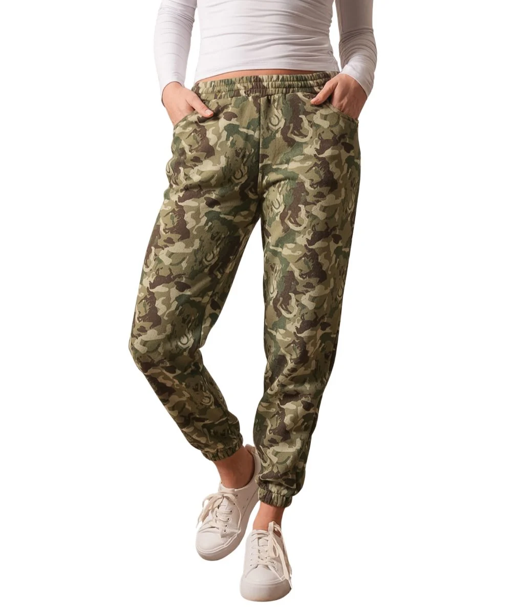 A person wearing camouflage jogger pants with an elastic waistband and cuffs, paired with a white long-sleeve top and white sneakers, shown against a plain white background.