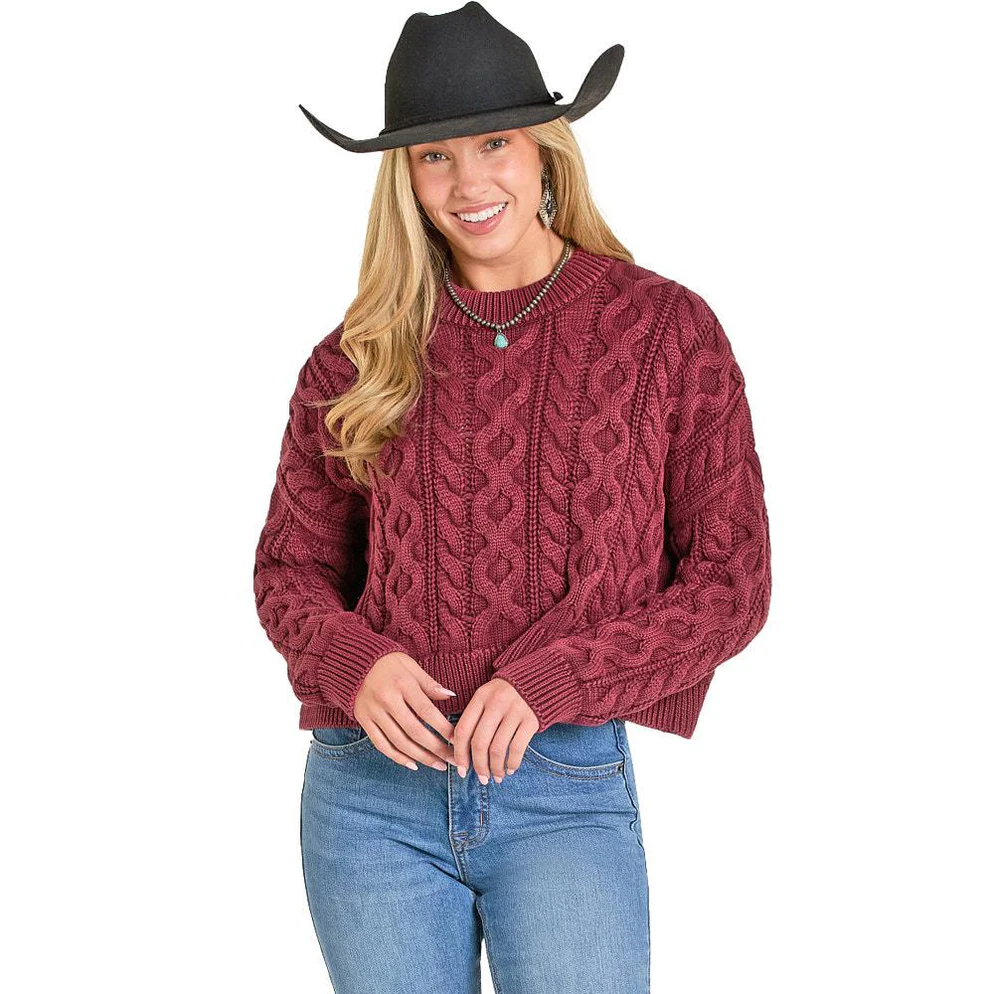 Woman wearing a burgundy cable knit sweater, blue jeans, and a black cowboy hat 