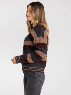 A woman wearing a long-sleeve crewneck sweater with horizontal stripes in dark brown, tan, and charcoal gray