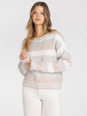 A woman wearing a textured, striped knit sweater in shades of beige, cream, and Grey