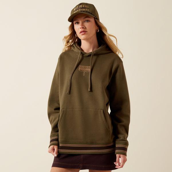 A woman wearing an olive green pullover hoodie with drawstrings, a kangaroo pocket, and ribbed cuffs and hem with thin tan stripes. 
