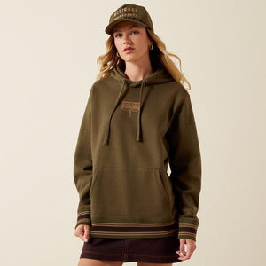 A woman wearing an olive green pullover hoodie with drawstrings, a kangaroo pocket, and ribbed cuffs and hem with thin tan stripes. 