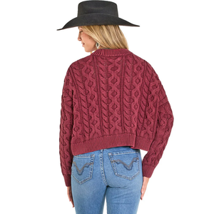 Woman wearing a burgundy cable knit sweater, blue jeans, and a black cowboy hat 