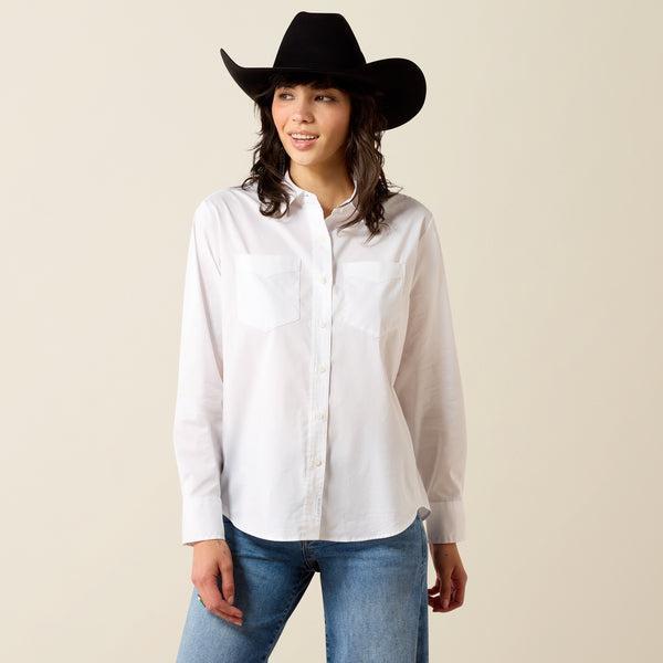 A woman wearing a white long-sleeve button-up shirt and a burgundy cowboy hat, looking down against a plain beige background.