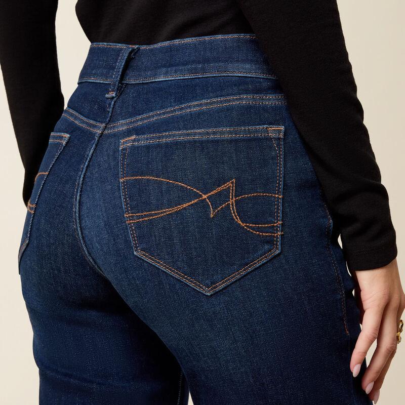 Close-up back view of a person wearing dark blue denim jeans with a black long-sleeve top, showing the back pocket and decorative orange stitching.