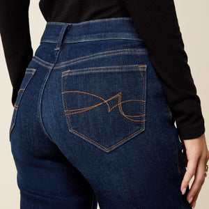 Close-up back view of a person wearing dark blue denim jeans with a black long-sleeve top, showing the back pocket and decorative orange stitching.