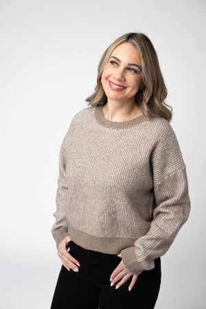 A woman wearing a beige ribbed knit crewneck sweater 