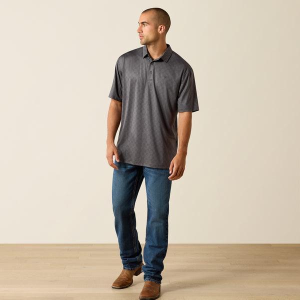 Man wearing a gray polo shirt and blue jeans standing against a plain background