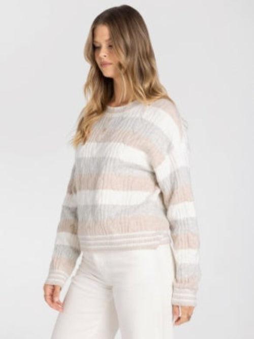 A woman wearing a textured, striped knit sweater in shades of beige, cream, and Grey