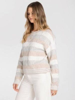 A woman wearing a textured, striped knit sweater in shades of beige, cream, and Grey