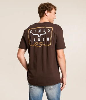 A man wearing a dark brown t-shirt with a large 'Kimes Ranch' logo printed on the back