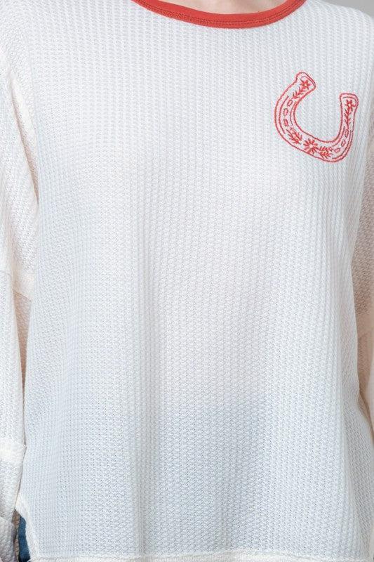 White textured shirt with red horseshoe emblem on a plain background
