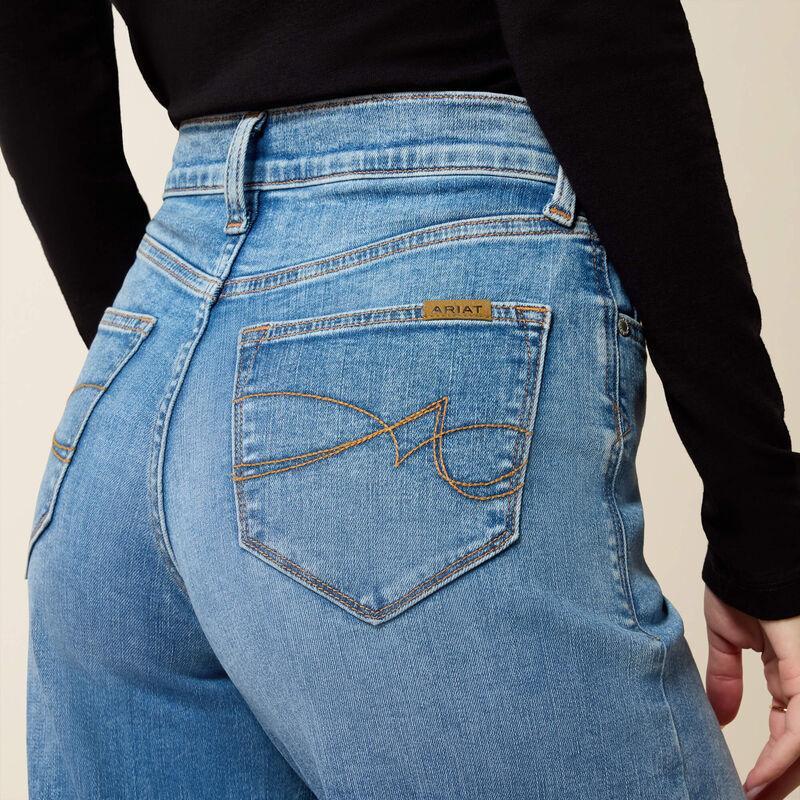 Close-up back view of a person wearing light blue denim jeans with a black long-sleeve top, showing the back pocket and a small visible Suits or similar brand tab on the pocket.