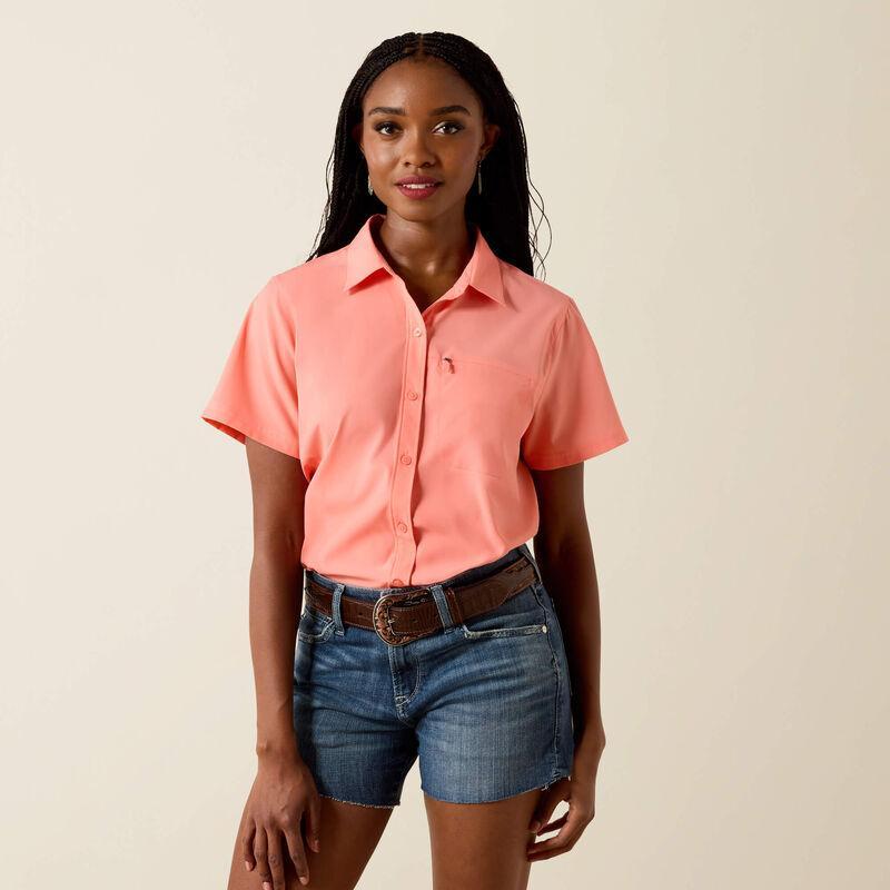 Woman wearing a coral shirt and denim shorts on a beige background