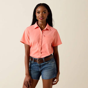 Woman wearing a coral shirt and denim shorts on a beige background