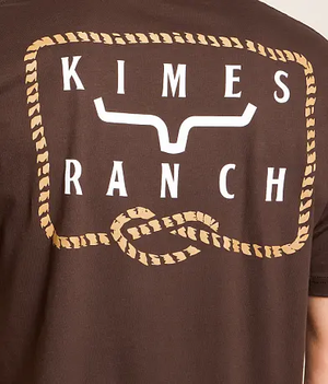 Close-up of a brown short-sleeve T-shirt showing the back graphic with the words 'KIMES RANCH' in white, a white steer skull graphic, and a tan rope-style border.
