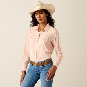 Woman wearing a PEACH shirt, blue jeans, and a beige cowboy hat on a plain background
