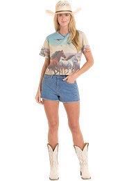 Woman wearing a cowboy hat, patterned shirt, denim shorts, and white cowboy boots on a white background
